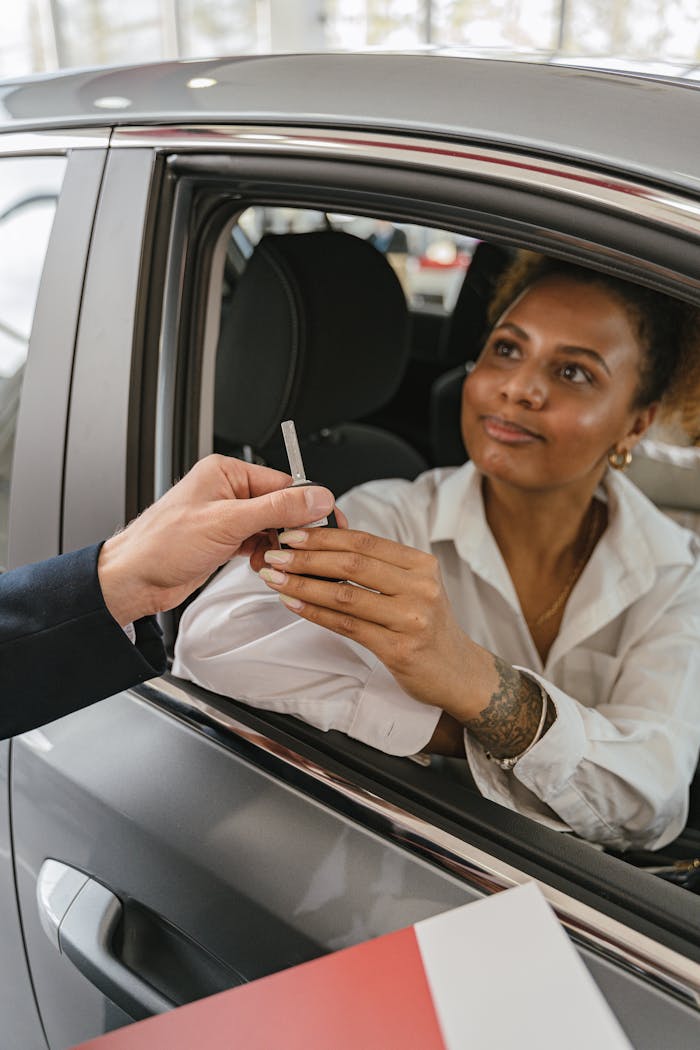 A woman in a car receives keys from a salesperson, symbolizing a new vehicle purchase.